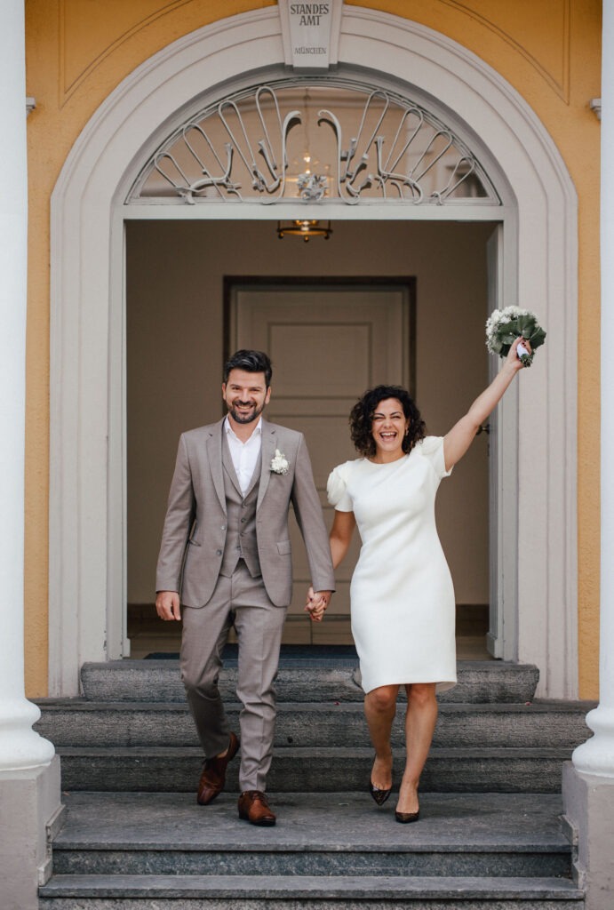 Brautpaar zieht aus Standesamt Mandlstraße München aus, mit viel Freude über ihre standesamtliche Hochzeit in München